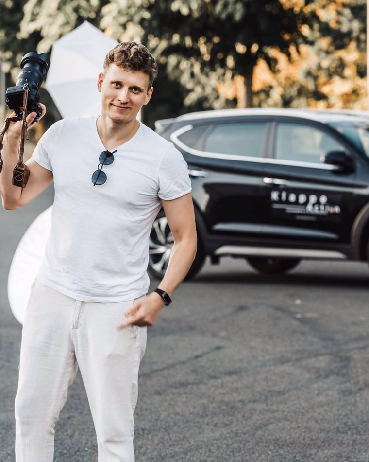 Clemens Zocher mit Kamera vor dem Wagen, unterwegs zu einem Termin