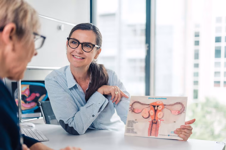 Ärztin erklärt einer Patientin am Schreibtisch eine anatomische Tafel
