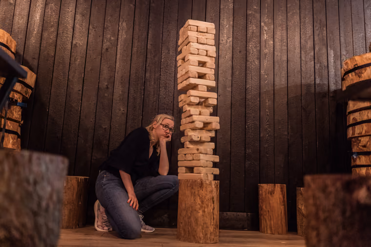 Frau kniet nachdenklich neben einem hohen Turm aus Holzklötzen